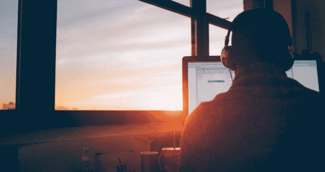 Man vor mit Kopfhörern vor Laptop bei Sonnenuntergang