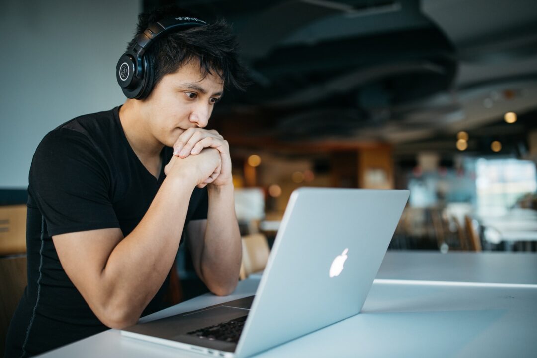 man met koptelefoon terwijl hij op stoel zit voor MacBook