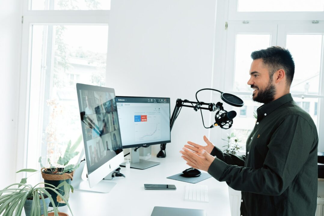 Mann in schwarzer Jacke vor Computer hält Presentation mit Untertiteln